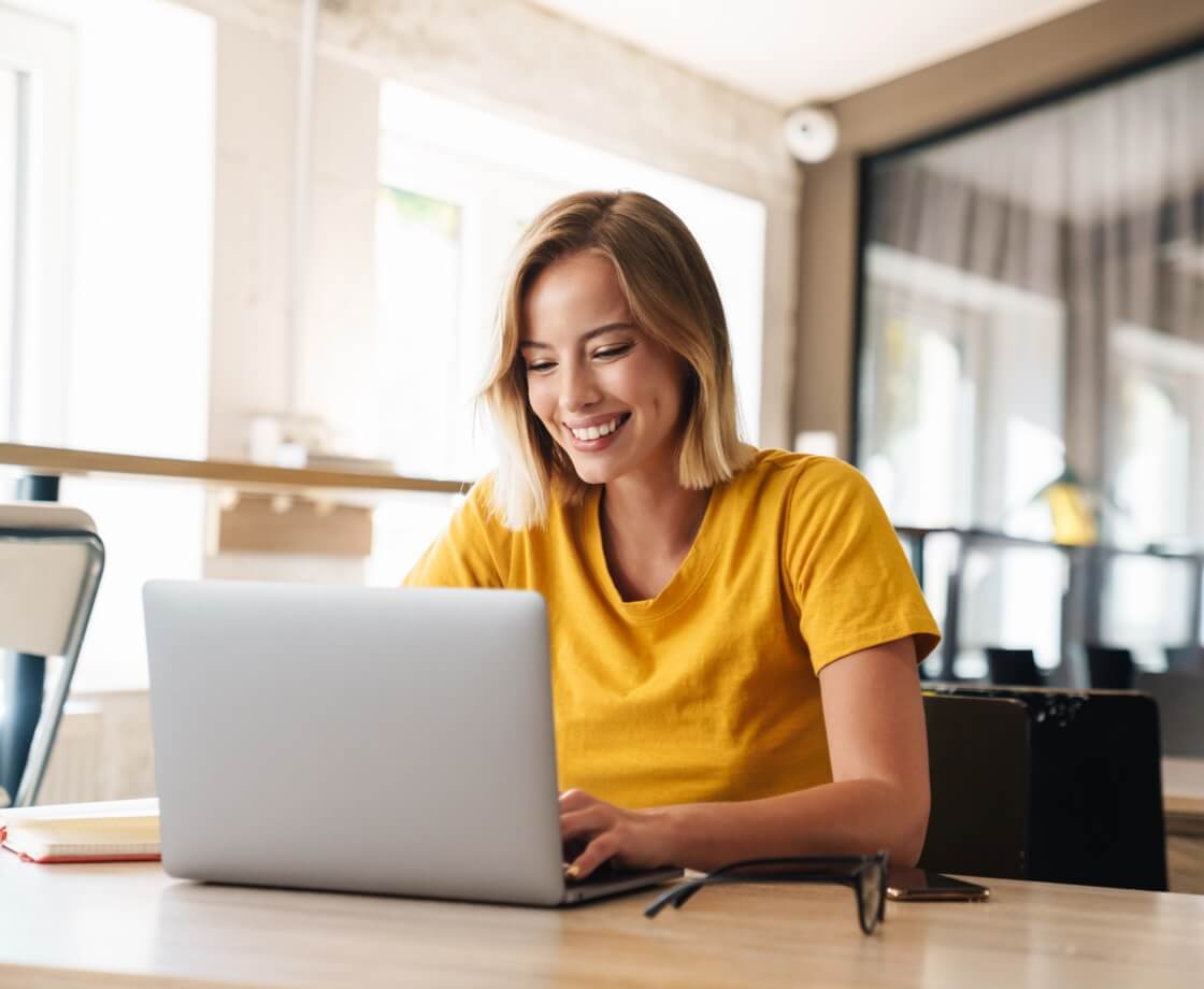 _photo-of-joyful-nice-woman-using-laptop-and-smiling-while-sitting